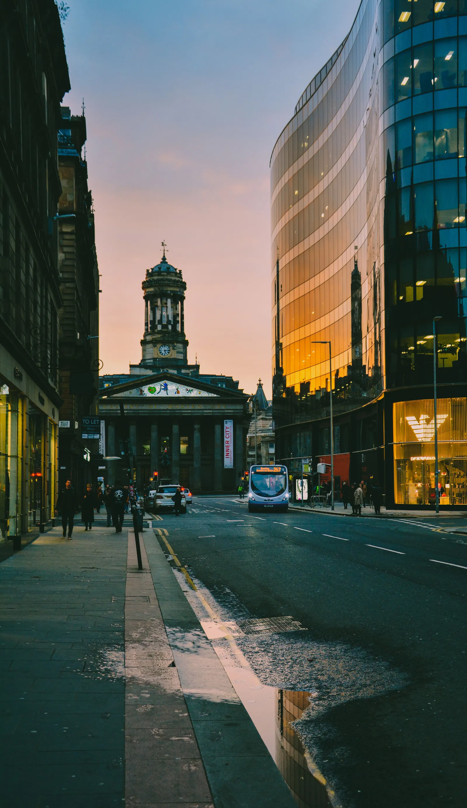 The Gallery of Modern Art at the end of Ingram Street in Glasgow at dusk, a bus approaching along the wet road